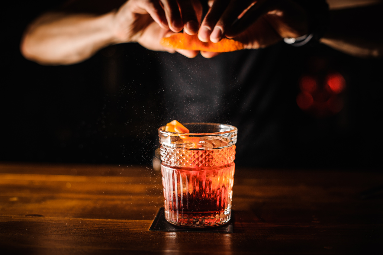 bartender with cocktail and orange peel preparing cocktail at bar